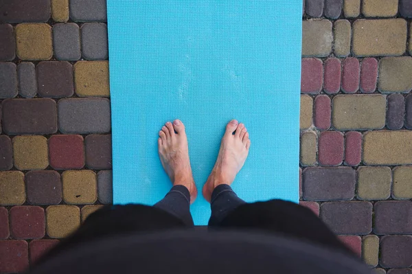 Directly above feet of an active man, sportsman, a yogi standing barefoot on a blue mat while practicing yoga outdoors. Copy advertising space. Active healthy lifestyle. Fitness. Sport. Workout