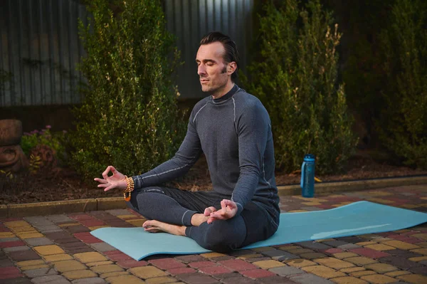 stock image Handsome peaceful confident male athlete, a man yogi with rosary beads, meditating in lotus pose on a yoga mat at sunset. Sunset sunlight. Yoga practice. Meditation. Mindfulness. Enlightenment