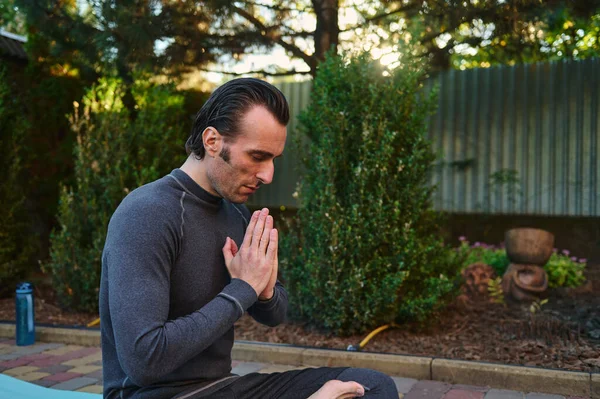 Close-up of a man athlete, a yogi meditating in lotus pose on a fitness mat, keeping hands palms together, practicing yoga at sunset. Spiritual growth. Meditation. Mindfulness. Enlightenment. Fitness