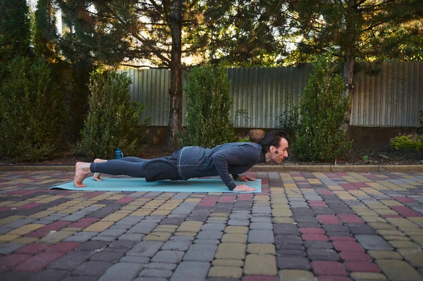 stock image Side portrait of an active athlete Caucasian man yogi in his 40s, doing Yoga chaturanga push-ups on a fitness mat while practicing outdoors. Sport Fitness workout. Active and healthy lifestyle