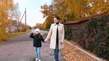 Çok ırklı, mutlu genç bir kadın, şefkatli bir anne ve güzel, sıcak bir sonbahar gününde sokakta yürürken el ele tutuşan sevimli küçük kızı. Kuru yapraklar düşer. Hint Yazı.