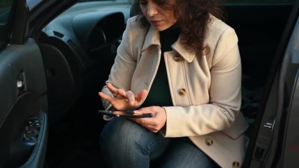 关注穿着休闲装 坐在停车场司机座位上 使用智能手机 查看新闻资料 浏览网站 拨打汽车服务电话的女性 — 图库视频影像