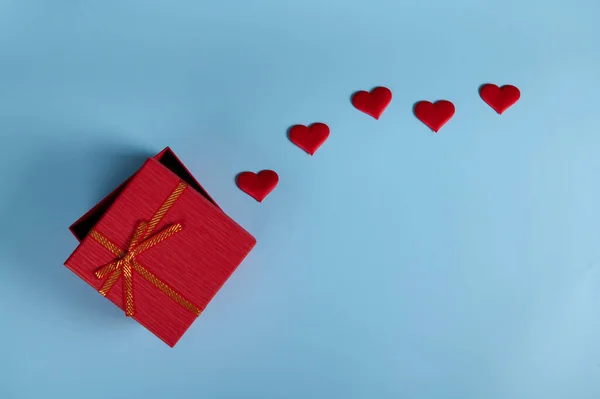 平躺在床上静谧的生活充满浪漫的惊喜 在半开着的红色礼品盒里 系着金色的蝴蝶结和红色的装饰心 隔离在淡蓝色的背景上 还有复制的广告空间 情人节 — 图库照片