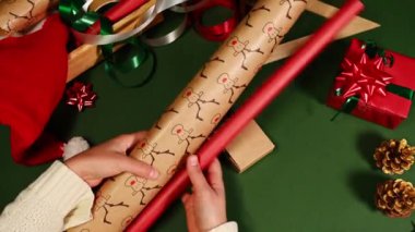 Yeşil yüzeyde noel ya da yeni yıl hediyelerini paketlerken ambalaj kağıdı ve dekoratif kurdele tutan kadınların üst görüntüsü. Xmas hazırlıkları. Boks günü. İyi tatiller. Kutlama