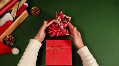 Üst manzarayı kapatın. Bej renkli, sıcak kazaklı bir kadın, yeşil bir masaya Xmas hediyelerini bire bir koyuyor. Mutlu Noeller ve mutlu yıllar konsepti. Boks Günü. Kutlama etkinlikleri için hediye paketleme