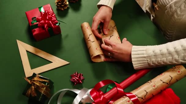 女性の手のクローズアップは 緑の表面に鹿のパターンで包装紙に小さな贈り物を包む メリークリスマスとハッピーニューイヤーのコンセプト クリスマスの準備だ 梱包用のプレゼント ボクシングの日 — ストック動画