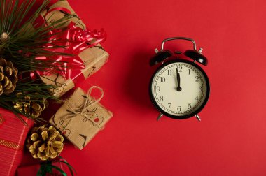 Düz yatıyordu. Gece yarısı aranan siyah antika çalar saat, kırmızı arkaplanda izole edilmiş Noel hediyeleri, kurdeleler ve yaylarla süslenmiş ve köknar ağacı dallarıyla süslenmiş altın çam kozalakları. Uzayı kopyala