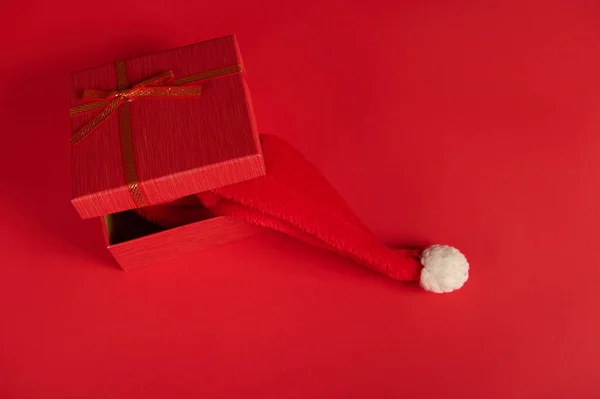 顶部是半打开的时尚红色礼品盒 用红色的蝴蝶结捆着 里面有一顶圣诞礼帽 在明亮的红色背景上与复制的广告空间隔离 新年和圣诞节的准备工作 节礼日 — 图库照片