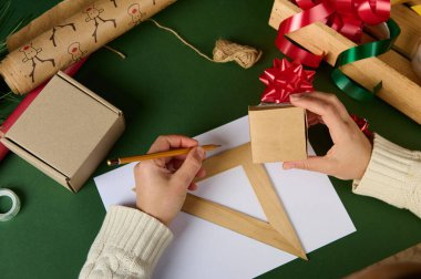 Üst görüşlü kadınların elleri, karton kutular, Noel, kadınlar, Sevgililer Günü veya ahşap cetvel ve kalem kullanarak herhangi bir olay için hediye paketleme malzemesi miktarını hesaplar.
