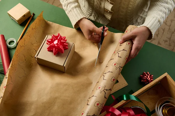 妇女在包装圣诞礼物 新年礼物或任何其他庆祝活动的礼物时剪下包装纸的头像 在绿色背景的木箱上的装饰磁带 节礼日 — 图库照片