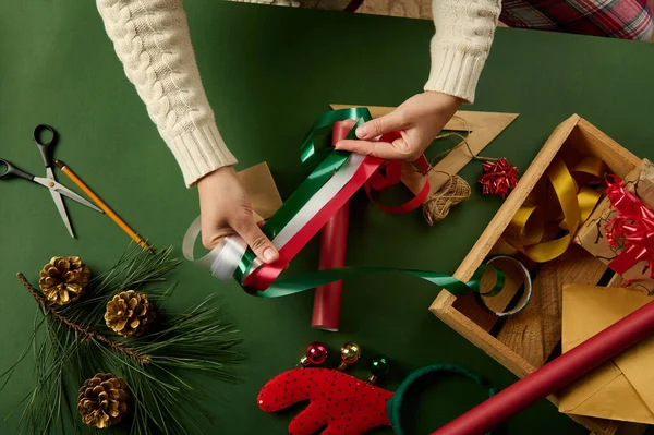 stock image Top view womans hands holding red, white and green shiny decorative ribbon over a background with wrapping materials, for packing gifts for Christmas, New Year or other celebration event. Boxing Day