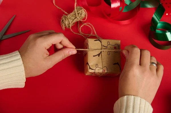 女人用亚麻绳把圣诞礼物绑在红色的背景上 四周都是喜庆的装饰品 包装纸 包装礼物 节礼日新年准备工作 — 图库照片