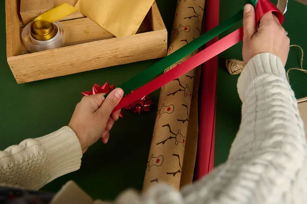 俯瞰女性的双手 在包装纸上贴上红色和绿色缎子装饰带 包装圣诞礼物或新年礼物 手工艺术 节礼日创意 — 图库照片