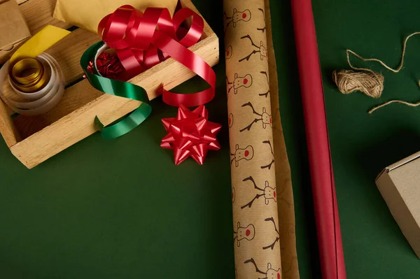 带有鹿纹和红色的特写包装纸 旁边是带有装饰带 缎带和绿色背景的木制板条箱 节礼日包装礼物 圣诞魔幻心情 — 图库照片