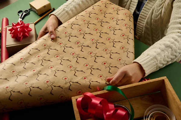 Selective focus on a wrapping gift paper with deer pattern in womans hands, packing presents for Christmas or New Year. Boxing Day. New Year and Xmas preparations. Happy winter holidays. Diy presents