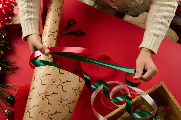 女性手拿起礼物带的特写镜头 贴在包装纸上 用红色背景包装圣诞礼物 四周是节日装饰和装饰品 — 图库照片