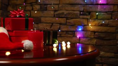 Noel arkaplanı şirin Noel ışıkları, Noel Baba şapkası ve ahşap bir masanın üzerinde renkli ışıklardan oluşan çelenklerle aydınlatılmış tuğla bir duvarın arkasında sunuluyor. Uzayı kopyala