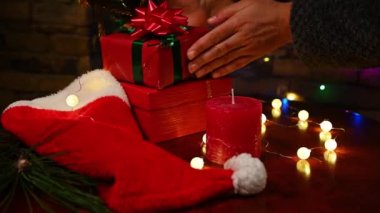 Kadınların eli, renkli çelenklerle aydınlatılmış, rahat bir iç mekânda, ahşap bir masaya Noel hediyeleri koyuyor. Yılbaşı ve Noel hazırlıkları evde. Büyülü festival atmosferi. Sıcaklık