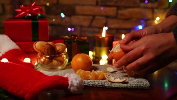特写女性的手清洁桌上新鲜多汁的橘子 为平安夜装饰 快乐的礼物 自制的烘焙饼干 圣诞帽和装饰着砖墙背景的装饰的花环 — 图库视频影像