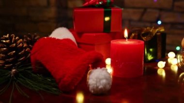 Sabit çekim: Yılbaşı ve Noel arifesi için Noel arkaplanı. Kırmızı mum, ev yapımı hamur işleri, hediye kutuları, köknar ağacının dalındaki çam kozalakları ahşap masanın dekoru.