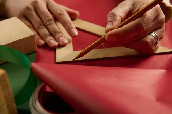 用木制三角形尺子在红色礼品纸上画特写 计算圣诞节 新年或任何其他节日礼物包装所需的包装材料数量 — 图库照片