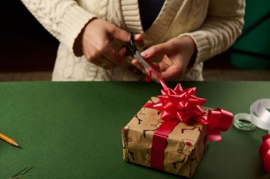 Yakın plan bir kadının elleri parlak kırmızı kurdelenin güzel kurdelesini bağlarken bir de Noel hediyesini süslüyor. Paketleme. Yeni yıl ya da başka bir kutlama etkinliği için paketleme hediyeleri. 25 Aralık. Boks Günü.