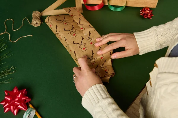 一个穿着米黄色毛衣的女人的头像 她把礼物包在一张可爱的装饰纸上 上面有鹿纹图案 绿色背景 复制广告空间 圣诞和新年的准备工作 节礼日 — 图库照片