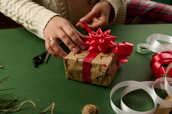 stock image Top view woman's hands tying beautiful bow from shiny red ribbon while decorating a Christmas gift. Wrapping. Packaging presents for New Year or any other celebration event. December 25th. Boxing Day.