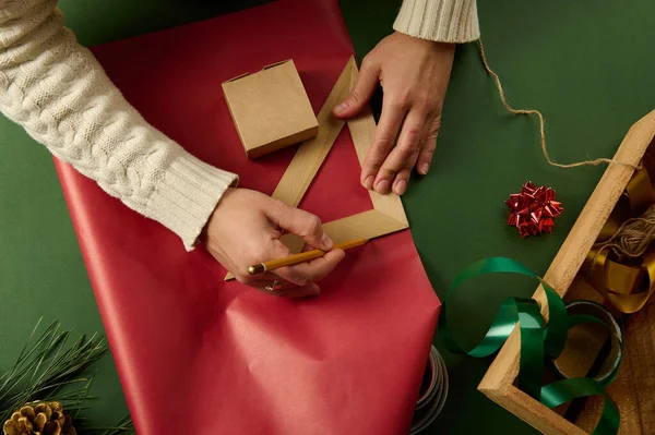 用木制铅笔和三角形尺子画在红色包装纸上的俯瞰女性的手 计算用来包装情人节 圣诞节或新年礼物的数量 — 图库照片