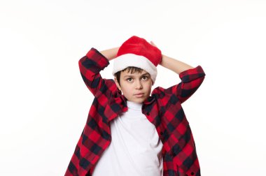 Kendine güvenen, düşünceli, Noel Baba şapkası takan, beyaz arka plan üzerinde poz veren ve kameraya bakan genç bir çocuğun izole edilmiş portresi. Reklam alanı. Mutlu noeller. Xmas. Sihirli kış