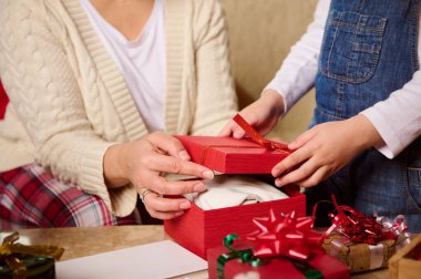 Ayrıntılar: Bir kadının elleri - anne ve çocuk - kız güzel kırmızı hediye kutusunda hediyeler paketliyor. Mutlu sihirli Noel atmosferleri. Yeni yıl hazırlıkları. Kış tatili atmosferi