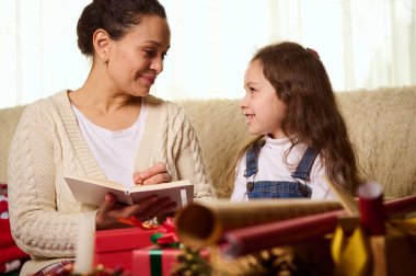 Mutlu aile kavramı. Sevecen anne ve sevimli kızı Noel hediyesi listesi yapar, mutlu bir şekilde gülümser, birbirlerine bakar, hediyeleri paketler, kış tatillerinde birlikte vakit geçirirler.