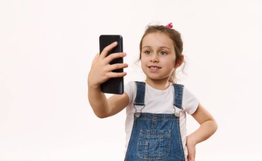 Küçük sevimli beyaz kız çocuğu cep telefonu kullanıyor, video bağlantısı üzerinden ailesiyle konuşuyor, reklam metinleri için kopyalama alanı olan beyaz arka planda izole edilmiş. Akıllı telefonda çevrimiçi sohbet