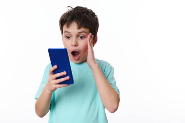 Kafkasyalı genç çocuk cep telefonu kullanıyor, haber okuyor, şok geçiriyor, şaşırıyor, şaşırıyor, şaşırıyor, beyaz arka planda izole edilmiş. Reklam metni için reklam alanını kopyala