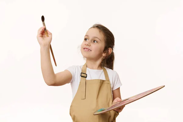 一个年幼可爱的小女孩拿着一副画的调色板 在镜头前拿着一把木制画笔 白色背景上的孤立的肖像 创意艺术发展与儿童娱乐 — 图库照片
