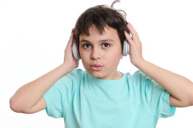 Yakından çekilmiş, çok ırklı turkuaz tişörtlü yakışıklı bir çocuk kablosuz kulaklık takıyor, kameraya bakıyor, reklam metinleri için reklam alanı olan beyaz arka planda izole edilmiş.