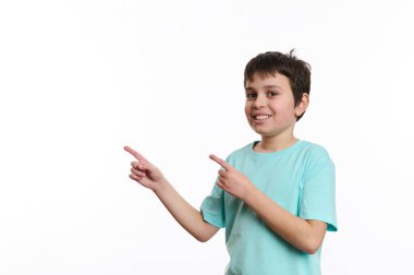 Zeki bir öğrencinin beyaz arka planında izole edilmiş bir portre. Mavi turkuaz tişört giyen neşeli bir genç. Promosyon metnin için reklam alanına işaret ederken sana bakıyor.