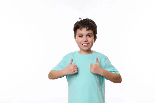 stock image Portrait of Caucasian handsome pleasant teenage child boy in blue casual t-shirt, smiling pleasantly, looking at camera, showing thumbs up, isolated on white background with space for promotional text