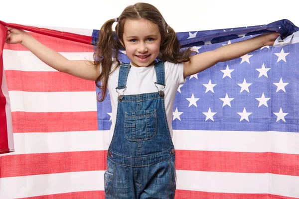Mutlu beyaz çocuk, mavi kot pantolon giyen, güzel dişli bir gülümsemeyle gülümseyen, uzanmış ellerinde Amerikan bayrağı tutan sevimli kız çocuğu. 4 Temmuz - Bağımsızlık Günü
