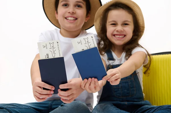 Selective focus on flight ticket or boarding pass in blurred traveler passenger kids hands near a yellow suitcase over white background. Travel. vacations. Journey. Flight. Space for advertising text