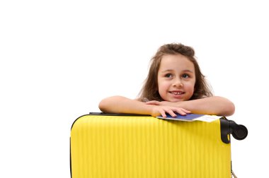 Adorable little passenger girl, with boarding pass and suitcase, traveling abroad for the weekend, smiling toothy smile, dreamily looking away at advertising space. Tourism Tourney Air travel concept clipart