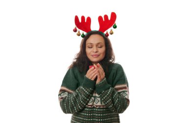 Geyik boynuzu halkası ve Xmas desenli yeşil kazak giyen çekici esmer kadın, mum ışığında gözleri kapalı poz veriyor, yaklaşan festival atmosferinin tadını çıkarıyor, beyaz üzerine izole edilmiş.