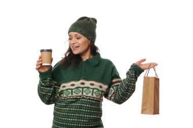 Sıcak yünlü yeşil şapkalı neşeli kadın ve Xmas desenli örgü süveter, elinde bir paket sıcak içecek ve kağıt torba taze yiyecek, ev servisinin rahatlığı, beyaz arka plan