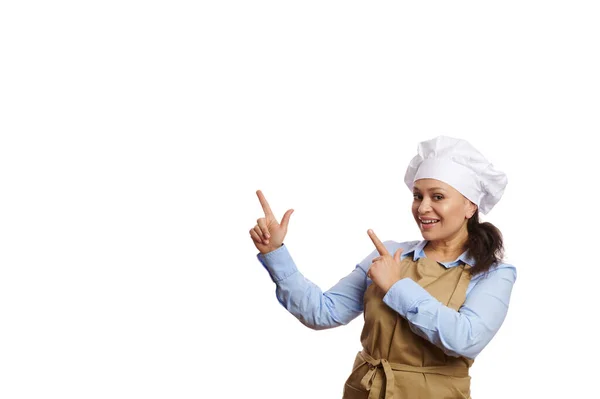 与白色背景隔离 美丽的多种族女性厨师 米黄色围裙上的厨师甜点师 用她的手指指向一个复制空间为您的广告文本 烹饪课的概念 — 图库照片