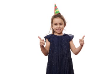 Zarif koyu mavi elbiseli neşeli beyaz bir çocuk, doğum günü kızı, gülümseyen, başparmaklarını gösteren, kameraya bakan, beyaz arka planda izole edilmiş, mesaj için bedava reklam alanı olan