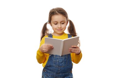 İki at kuyruklu, sarı ceketli, mavi kot pantolonlu, beyaz arka planda kitap okumaktan hoşlanan sevimli beyaz bir kız. Bilgi Bilgisi Eğitim Çocukları ve Okul Konsepti