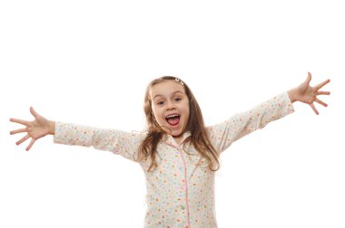 Kafkasyalı, pijamalı, kollarını kaldırıp, neşeli, dişlek bir gülümsemeyle beyaz arka planda izole bir şekilde kameraya bakan, aşırı neşeli, şen şakrak küçük kız çocuğu. Ücretsiz reklam alanı