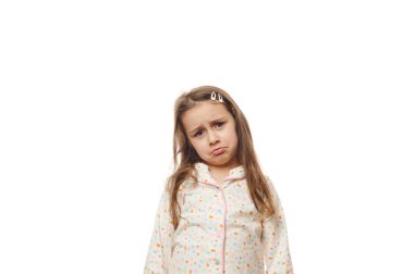 Üzgün, üzgün, uzun saçlı, beyaz pijamalı, üzgün, beyaz arka planda izole bir şekilde kameraya bakan küçük bir kız çocuğu. Yalnızlık, endişe ve umutsuzluk.