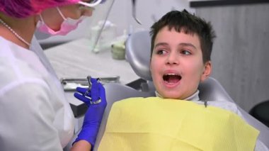 Teenage child boy patient getting a dental anesthesia, sitting on chair in dentistry clinic. Female dentist using stainless steel syringe, making anesthetic injection to her patient for pain relief