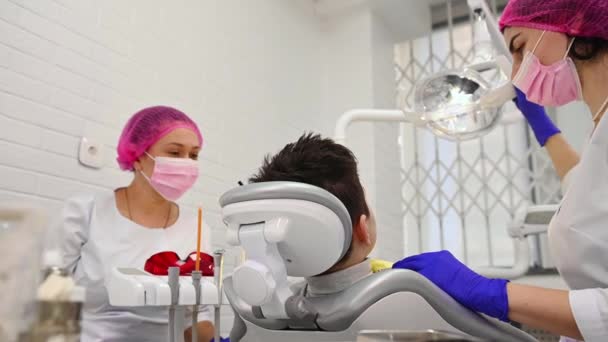 Bakifrån Tonårspojken Väntar Tandläkarundersökning Tandläkaren Hygienist Justera Lampan Innan Kontrollerar — Stockvideo